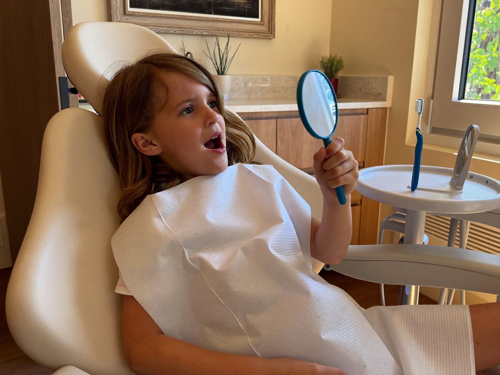 Curious child in the dental chair exploring a hand mirror